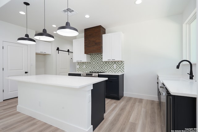 kitchen featuring a barn door, light hardwood / wood-style flooring, decorative light fixtures, and white cabinets