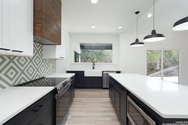 kitchen with light hardwood / wood-style flooring, hanging light fixtures, sink, white cabinets, and appliances with stainless steel finishes