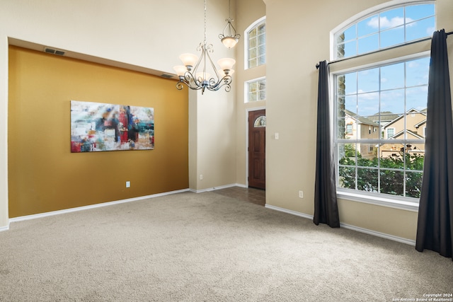 spare room featuring an inviting chandelier, plenty of natural light, a high ceiling, and carpet