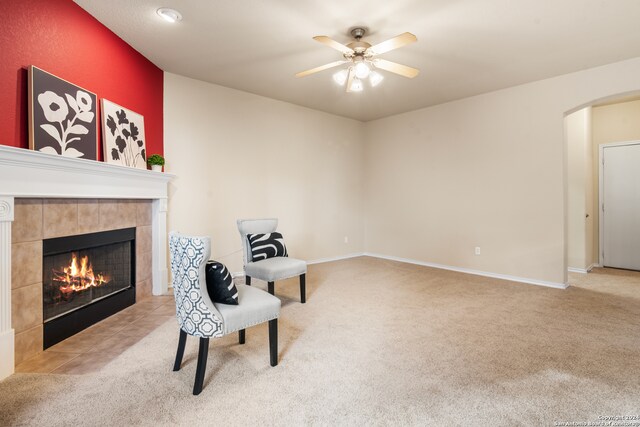 sitting room with a tile fireplace, light carpet, and ceiling fan