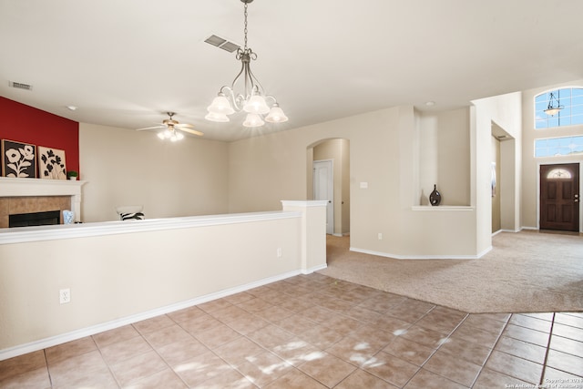 carpeted empty room featuring ceiling fan with notable chandelier and a tile fireplace