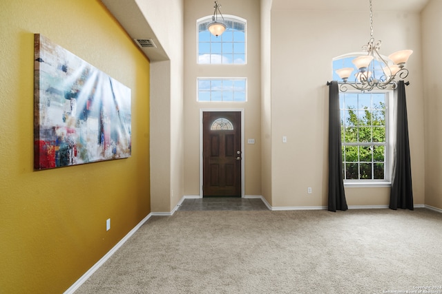 carpeted entryway with a healthy amount of sunlight, a high ceiling, and a chandelier