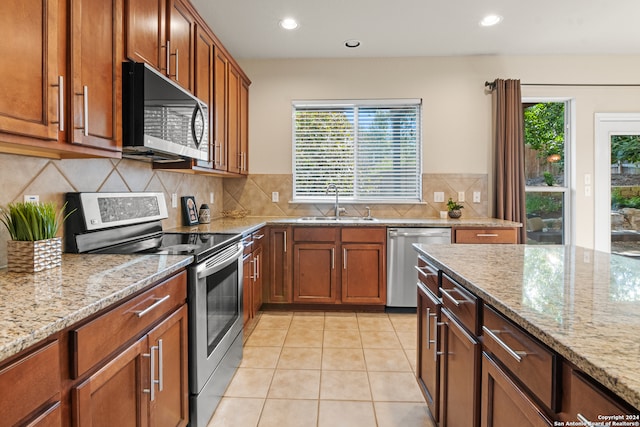 kitchen with tasteful backsplash, sink, stainless steel appliances, light tile patterned floors, and light stone countertops