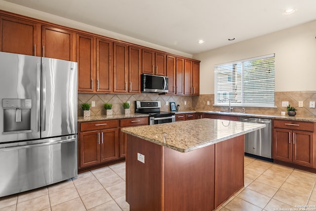 kitchen with appliances with stainless steel finishes, backsplash, a kitchen island, light stone countertops, and sink