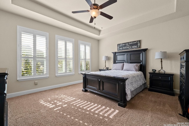 bedroom with ceiling fan, a tray ceiling, light carpet, and multiple windows