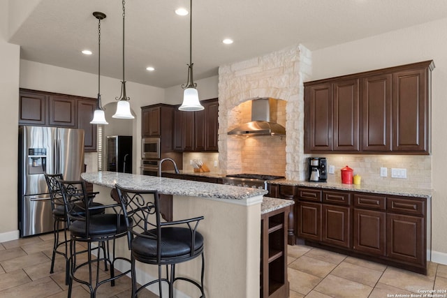 kitchen with decorative light fixtures, a center island with sink, wall chimney exhaust hood, stainless steel appliances, and decorative backsplash