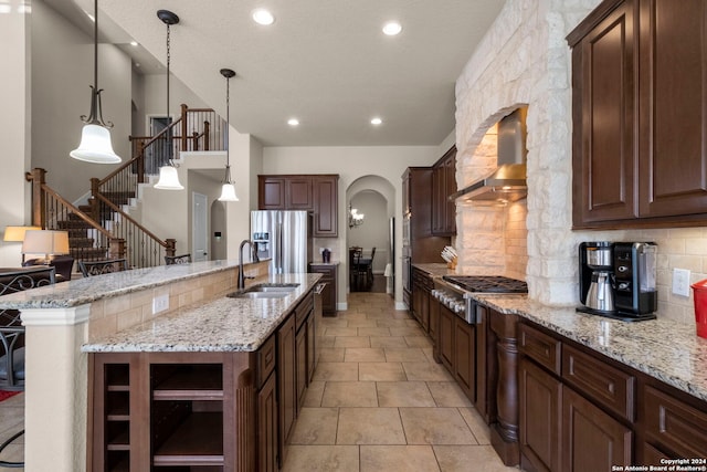 kitchen featuring a large island, sink, wall chimney range hood, appliances with stainless steel finishes, and decorative light fixtures