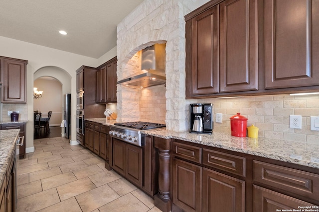 kitchen with stainless steel appliances, backsplash, light stone counters, and wall chimney range hood