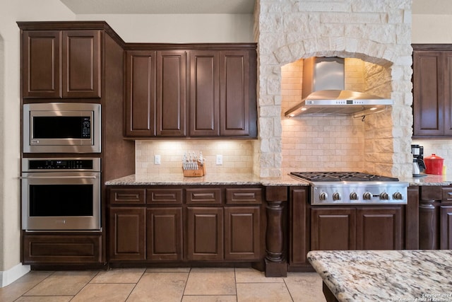 kitchen with wall chimney exhaust hood, stainless steel appliances, light stone counters, and tasteful backsplash