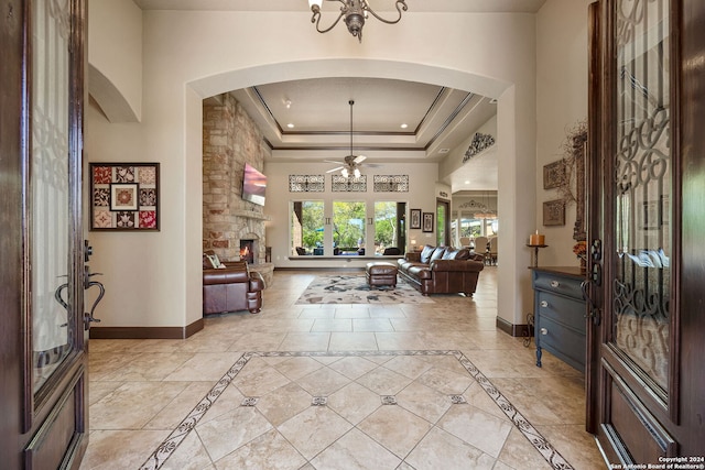 foyer with a stone fireplace, ceiling fan with notable chandelier, and a tray ceiling