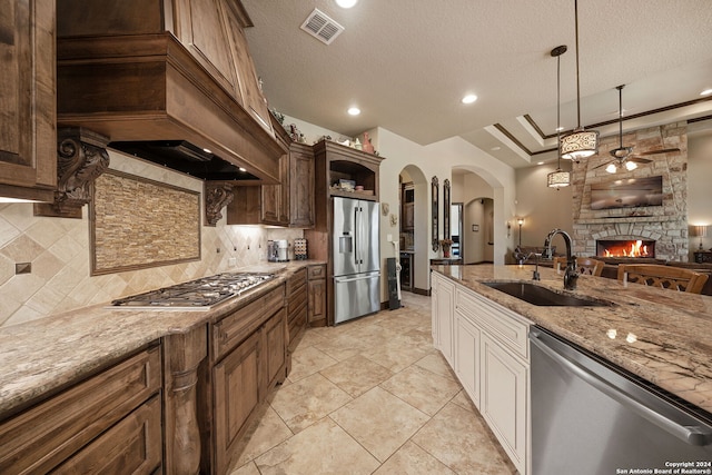 kitchen featuring ceiling fan, sink, a textured ceiling, stainless steel appliances, and a fireplace