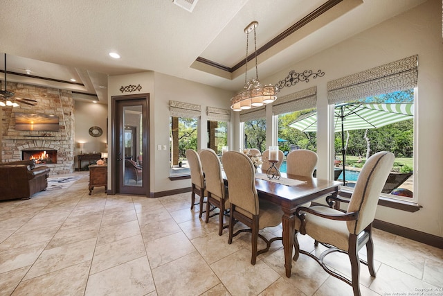 tiled dining room with a stone fireplace, a textured ceiling, a tray ceiling, ceiling fan, and ornamental molding