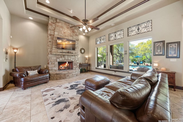 living room with light tile patterned flooring, a towering ceiling, a raised ceiling, a stone fireplace, and ceiling fan