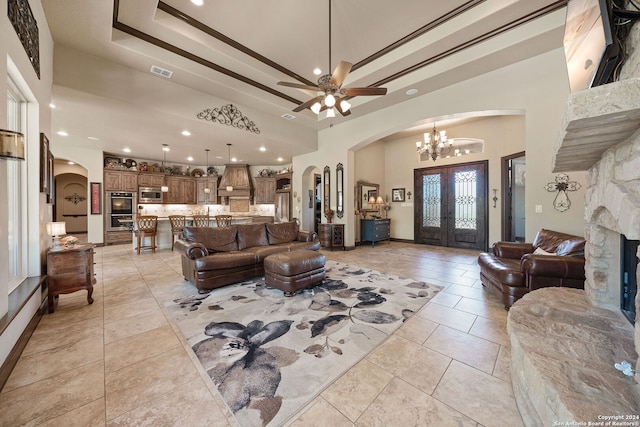 tiled living room featuring ceiling fan with notable chandelier, a fireplace, a towering ceiling, and a raised ceiling