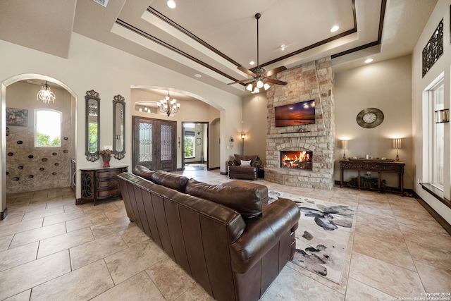 living room with a stone fireplace, ceiling fan with notable chandelier, a tray ceiling, and a high ceiling