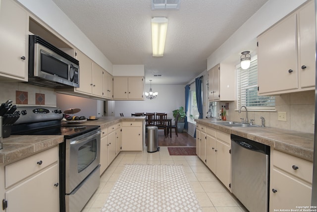 kitchen with appliances with stainless steel finishes, sink, hanging light fixtures, light tile patterned floors, and cream cabinets