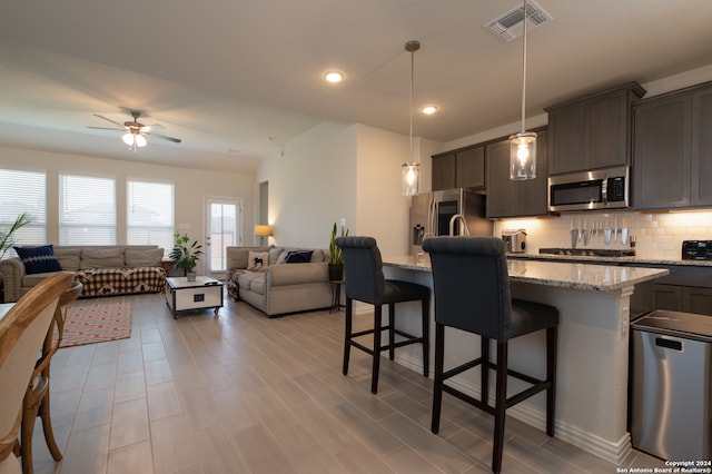 kitchen with hanging light fixtures, a breakfast bar, stainless steel appliances, ceiling fan, and a center island with sink