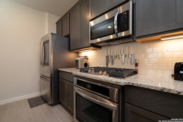 kitchen featuring appliances with stainless steel finishes, light stone counters, backsplash, light tile patterned floors, and dark brown cabinets