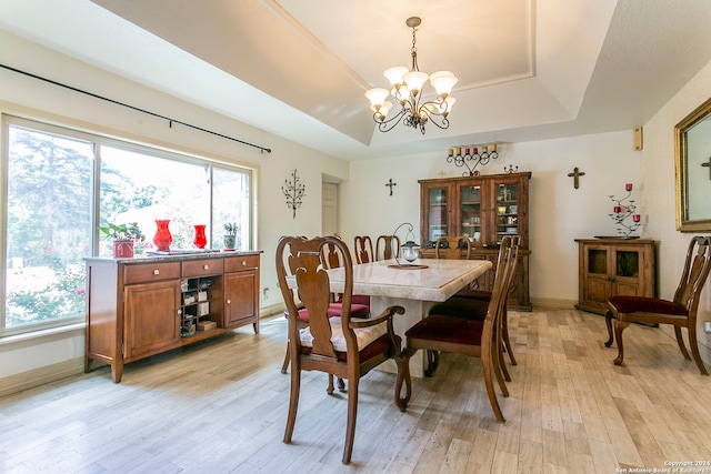 dining space with a tray ceiling, light hardwood / wood-style flooring, and a notable chandelier