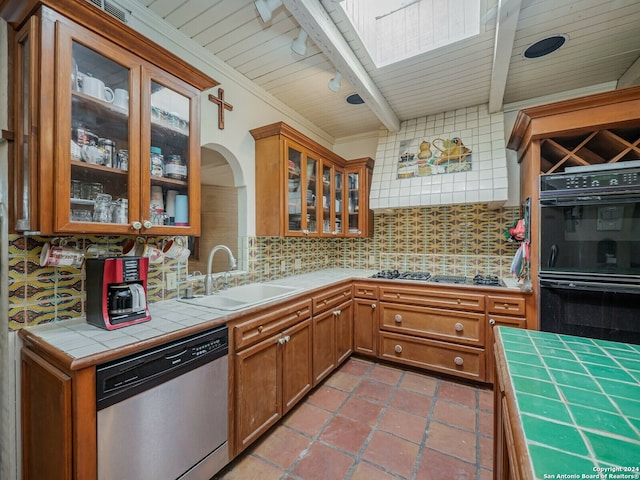 kitchen with beamed ceiling, a skylight, tasteful backsplash, stainless steel appliances, and tile counters