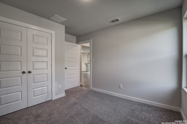 unfurnished bedroom with dark carpet, a textured ceiling, and a closet