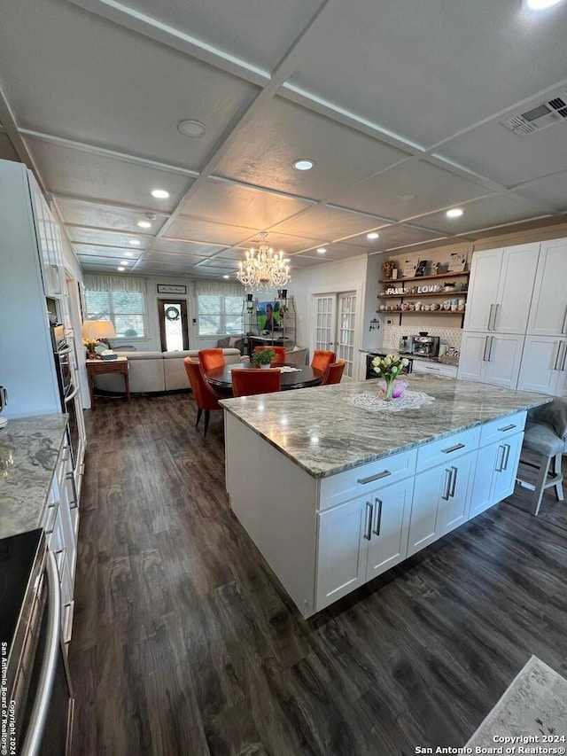 kitchen featuring white cabinetry, coffered ceiling, a spacious island, light stone countertops, and dark hardwood / wood-style flooring