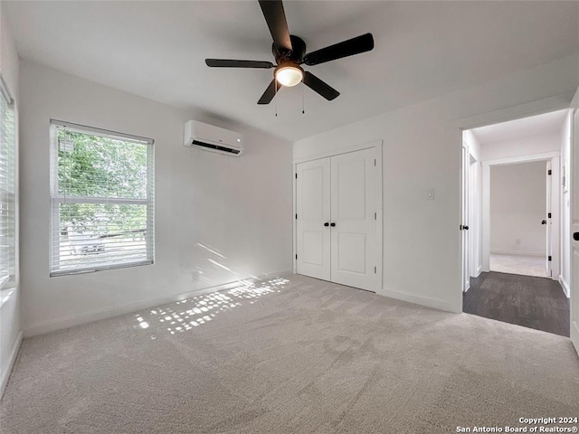 unfurnished bedroom with an AC wall unit, ceiling fan, light colored carpet, and a closet