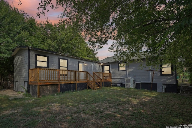 back house at dusk with ac unit, a wooden deck, and a lawn