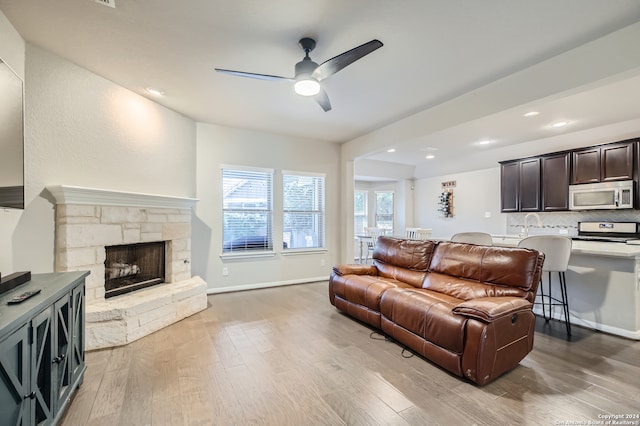 living room featuring ceiling fan, a stone fireplace, and light wood-type flooring