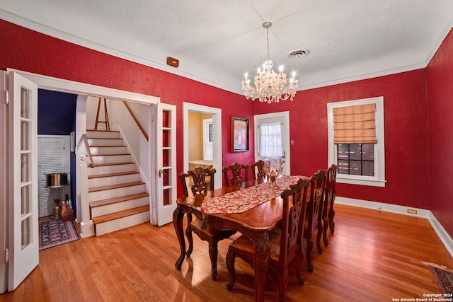 dining area with hardwood / wood-style flooring, ornamental molding, a textured ceiling, and an inviting chandelier