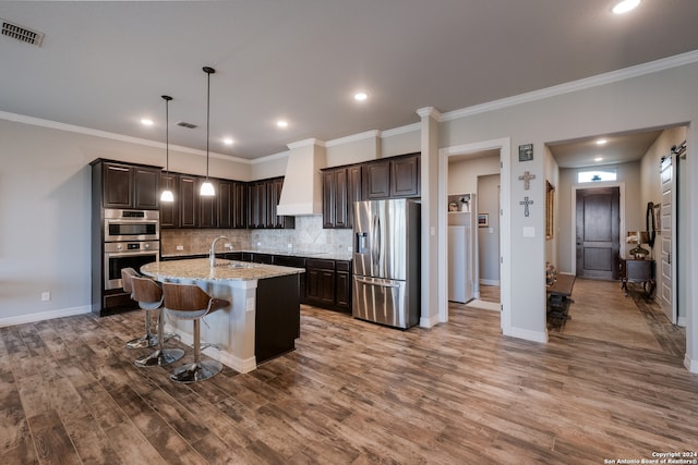 kitchen with light stone countertops, stainless steel appliances, hardwood / wood-style flooring, and a kitchen island with sink