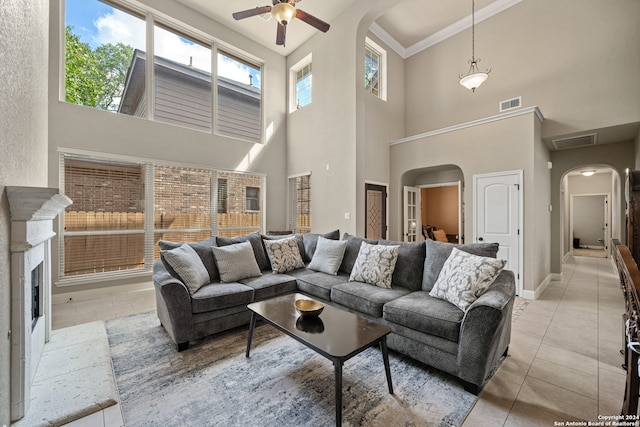 tiled living room featuring ceiling fan, ornamental molding, and a high ceiling