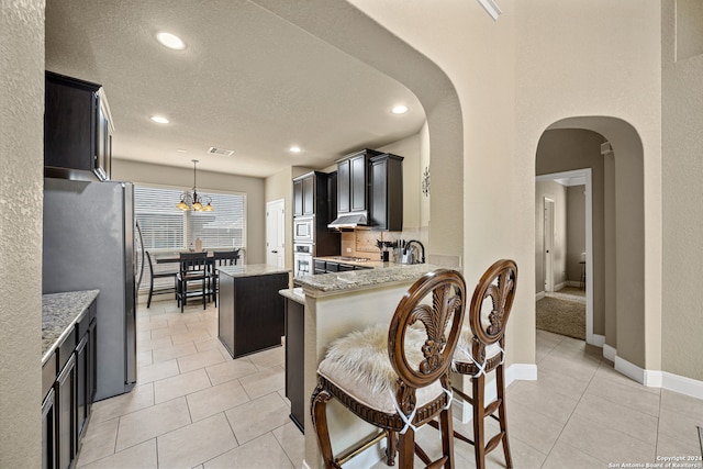 kitchen featuring appliances with stainless steel finishes, light stone counters, backsplash, pendant lighting, and a center island