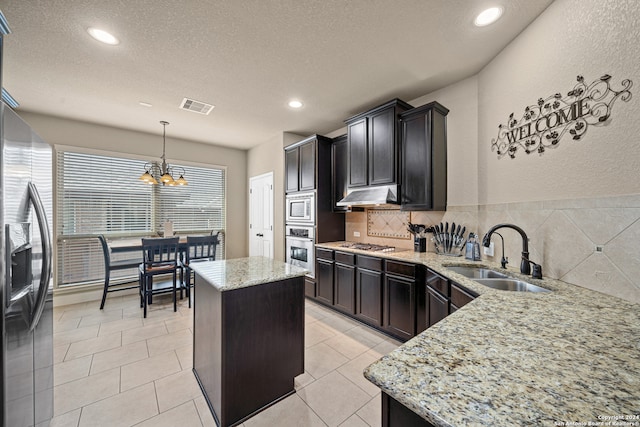 kitchen featuring a kitchen island, pendant lighting, stainless steel appliances, sink, and a chandelier