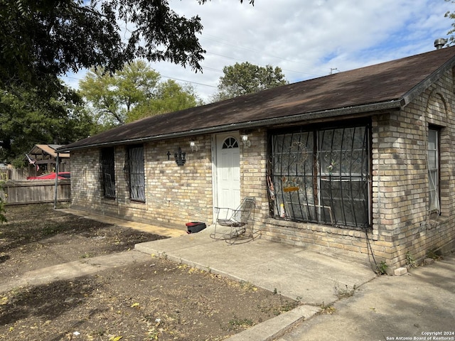 doorway to property featuring brick siding, fence, and roof with shingles