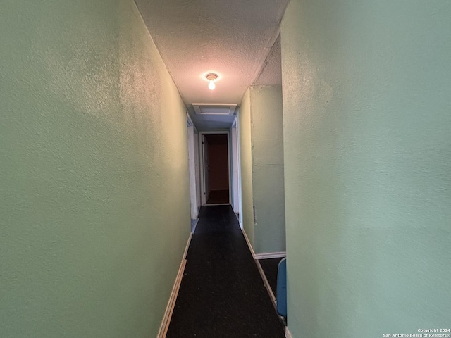 corridor featuring attic access, a textured ceiling, a textured wall, and baseboards