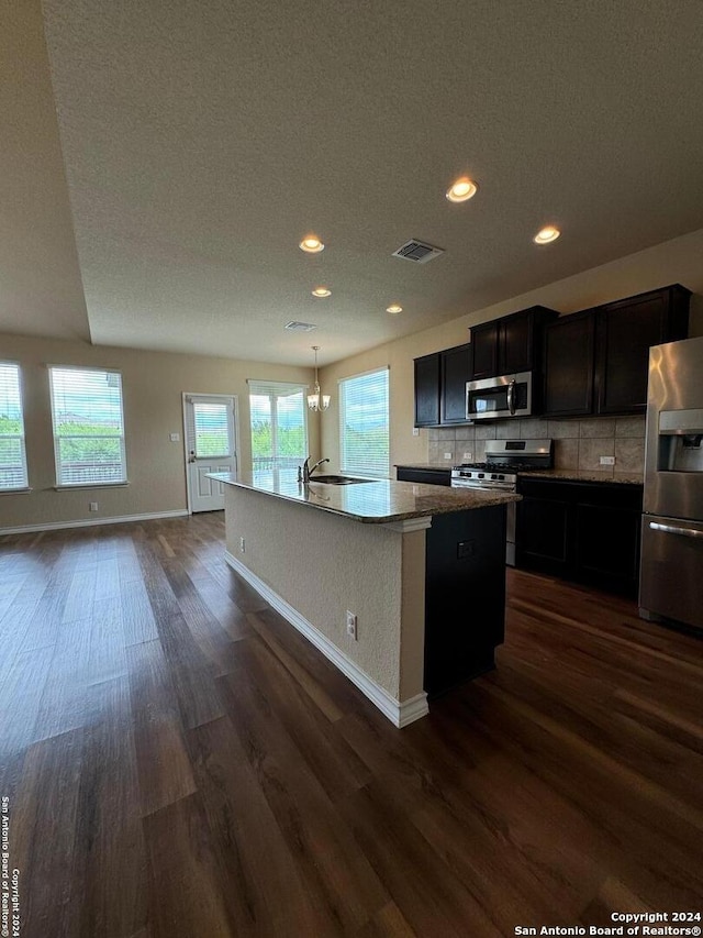 kitchen with appliances with stainless steel finishes, a center island with sink, dark hardwood / wood-style floors, and plenty of natural light