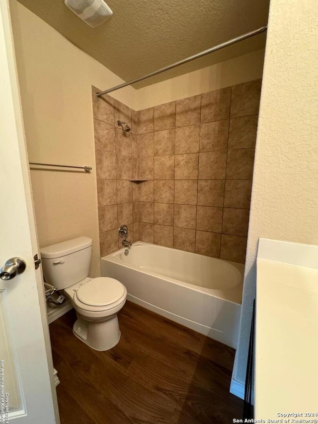 full bathroom featuring a textured ceiling, hardwood / wood-style floors, tiled shower / bath, vanity, and toilet