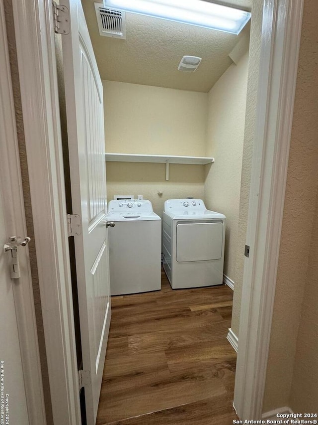 clothes washing area with hardwood / wood-style flooring, a textured ceiling, and washing machine and dryer