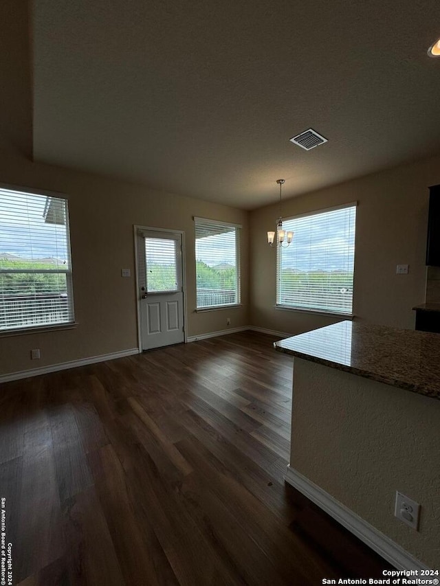 unfurnished living room featuring an inviting chandelier and dark wood-type flooring