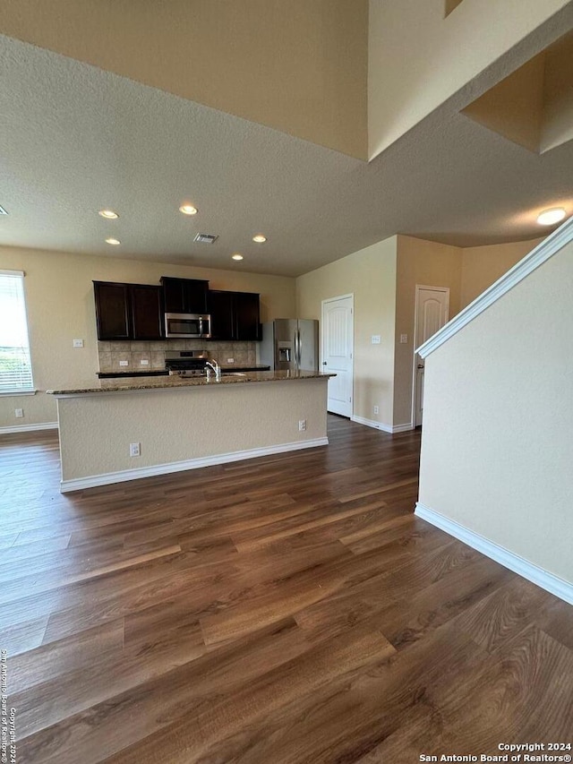 kitchen with an island with sink, appliances with stainless steel finishes, and dark wood-type flooring