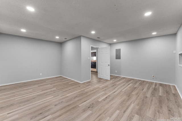 spare room with a textured ceiling, electric panel, and light hardwood / wood-style flooring