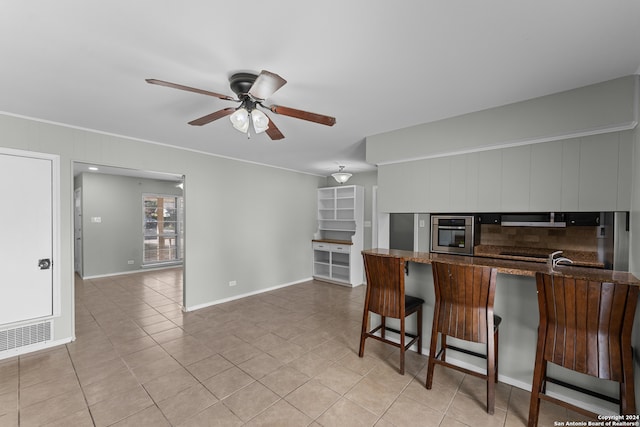 kitchen featuring kitchen peninsula, light tile patterned floors, stainless steel oven, ceiling fan, and dark stone counters