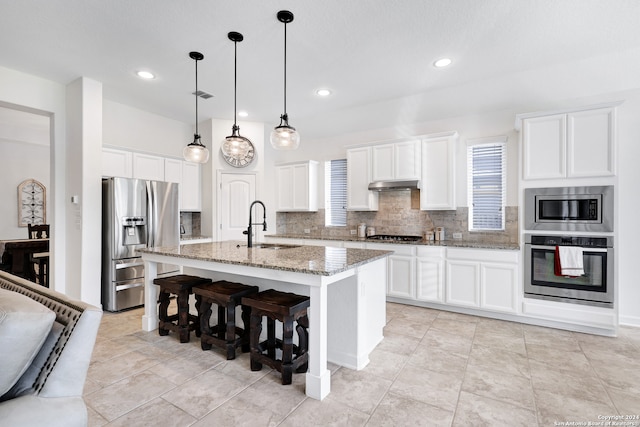 kitchen featuring a kitchen island with sink, light stone countertops, stainless steel appliances, and white cabinetry