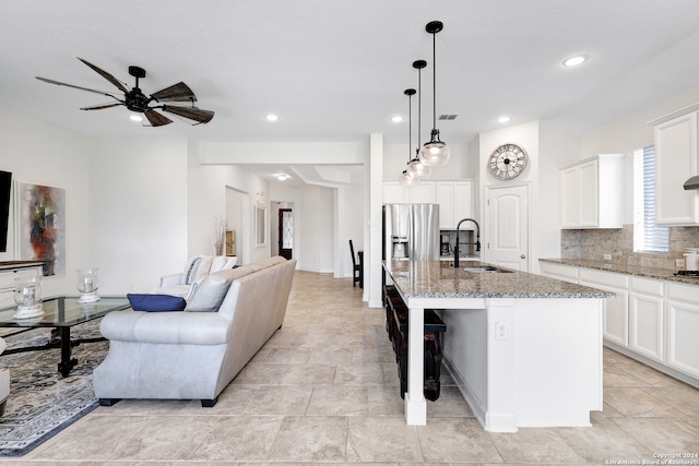 kitchen featuring pendant lighting, light stone counters, a kitchen island with sink, white cabinetry, and ceiling fan