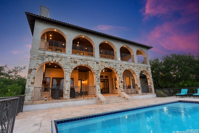 back house at dusk with a balcony, a fenced in pool, and a patio area