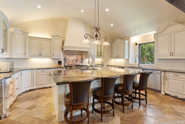 kitchen with hanging light fixtures, an island with sink, stone counters, stainless steel dishwasher, and sink