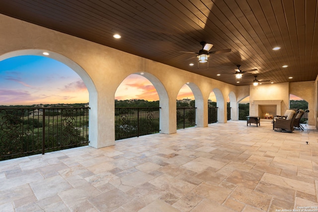 patio terrace at dusk with a large fireplace and ceiling fan