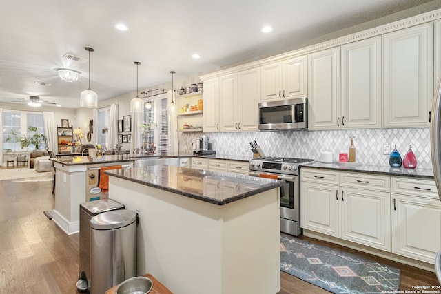 kitchen featuring a center island, kitchen peninsula, ceiling fan, stainless steel appliances, and decorative light fixtures