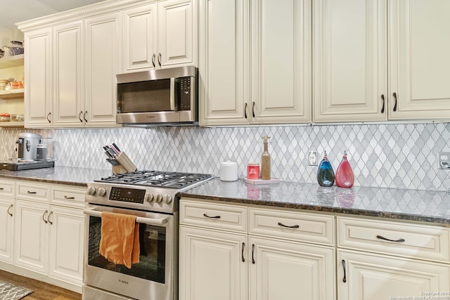 kitchen featuring wood-type flooring, stainless steel appliances, tasteful backsplash, and dark stone counters